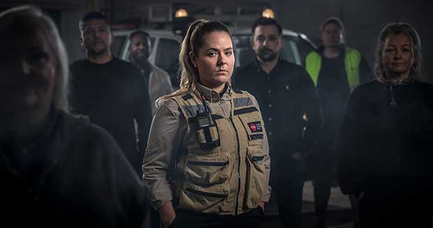 Kvinna ser in i kameran. Flera personer står runt omkring henne.